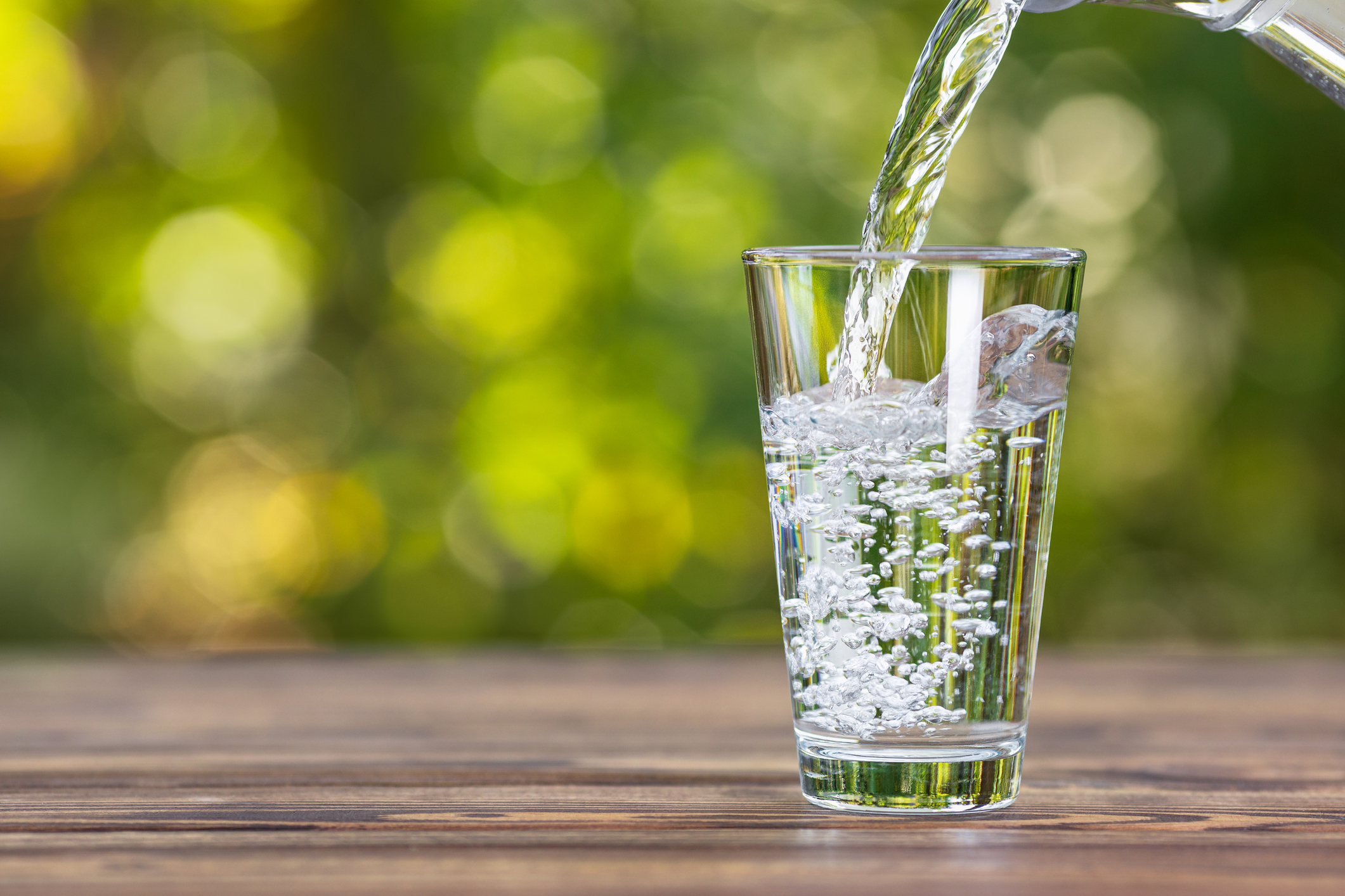 water from jug pouring into glass on wooden table outdoors