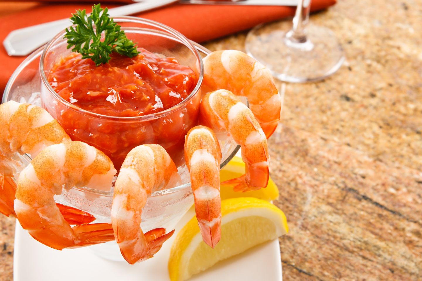 Cooked shrimp with cocktail sauce against a granite tabletop. Shellfish like shrimp are a delicious appetizer but also pose a health risk to anyone with a food allergy to shellfish.