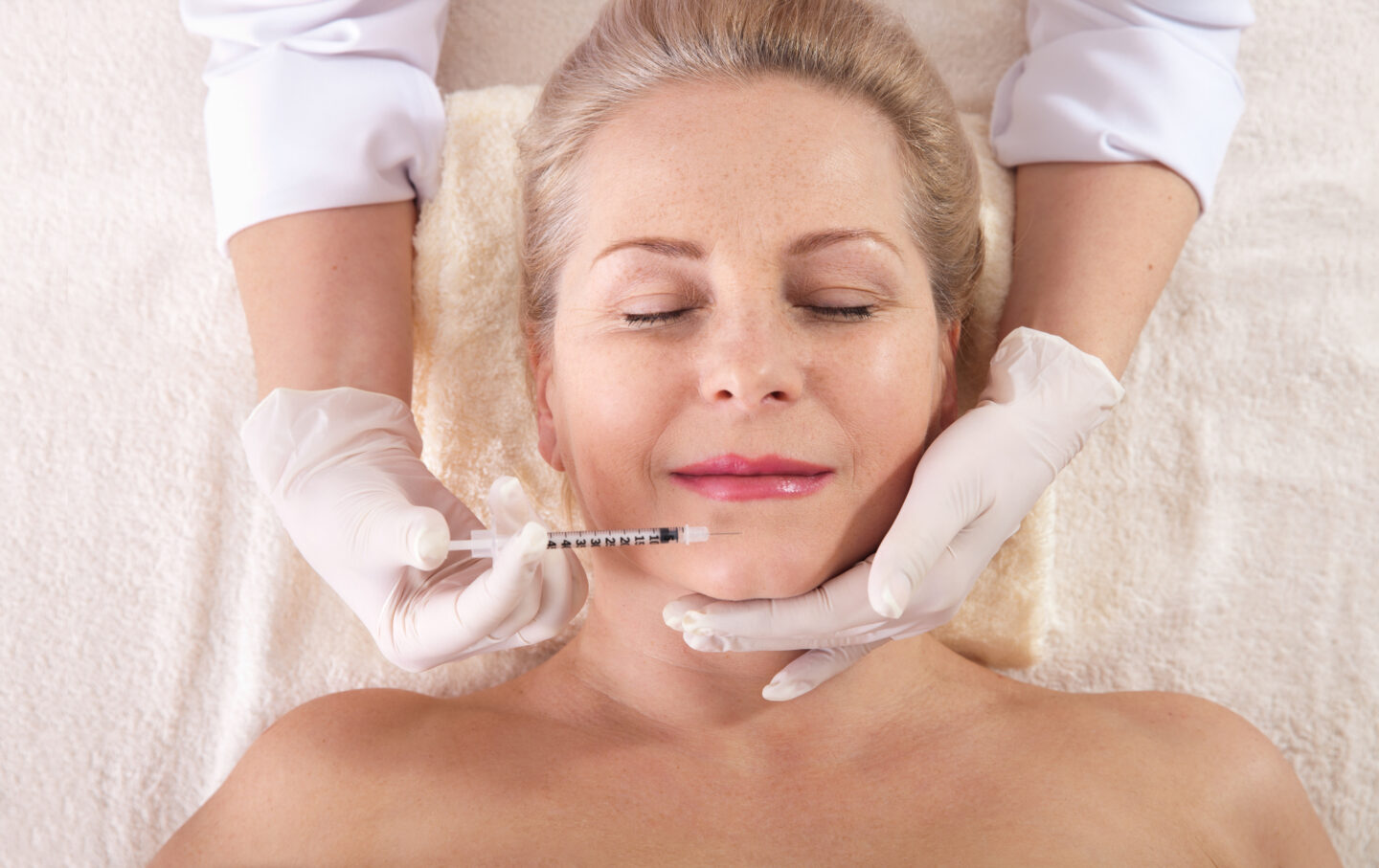 Middle aged woman gets cosmetic injection in her lips. Hyaluronic acid injection for facial rejuvenation procedure. Women in beauty salon. Plastic surgery clinic.