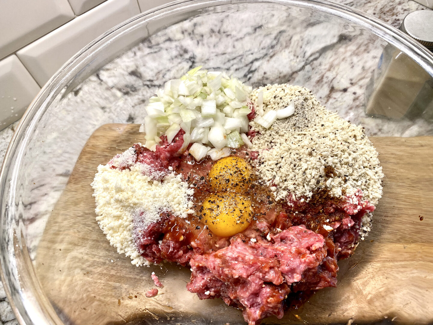  beef, onions, eggs, cheese and bread crumbs in a glass bowl ready for mixing.
