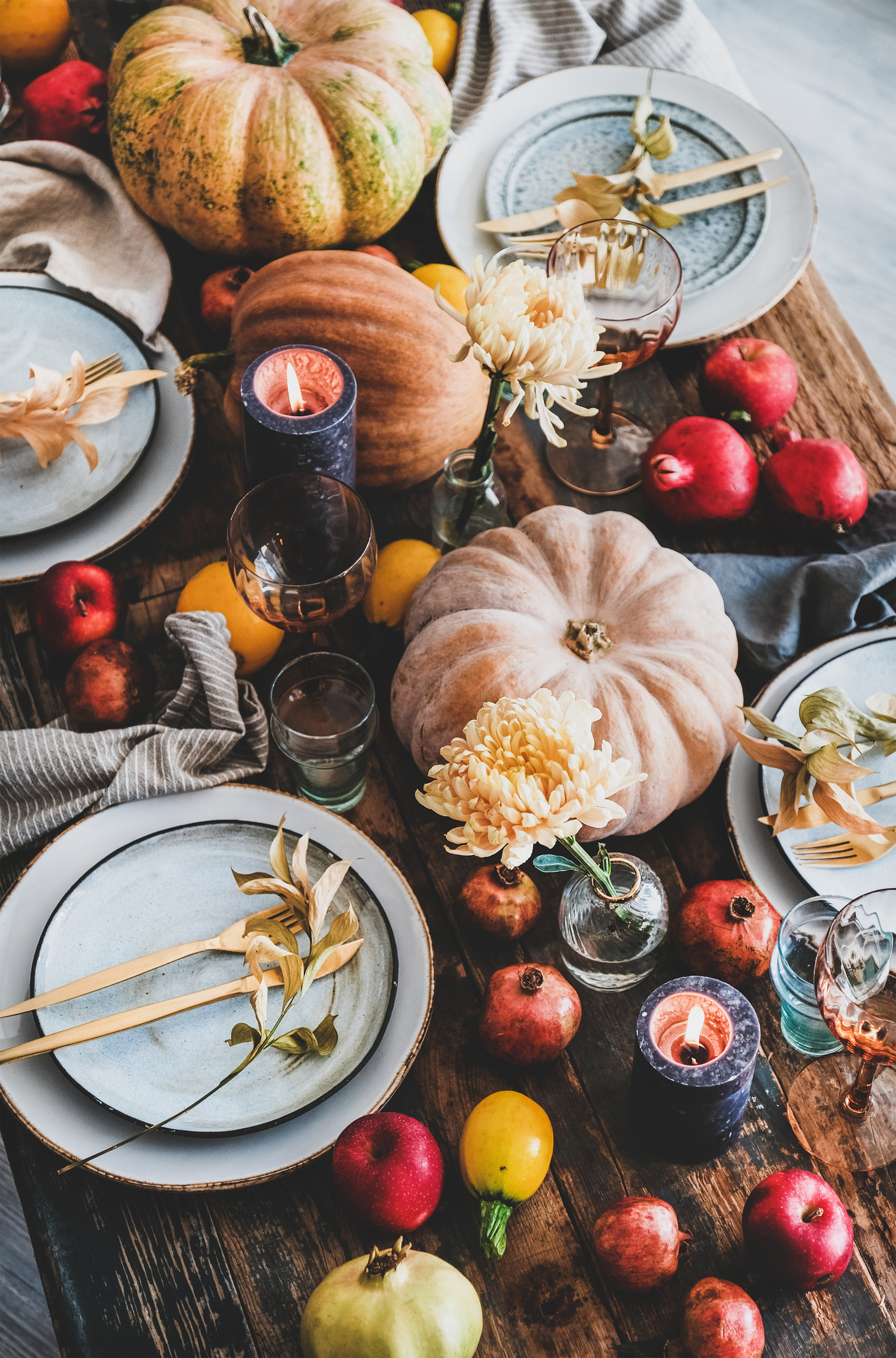 Fall table setting for Thanksgiving day party or family gathering dinner. Plates, silverware, floral and fruit decoration, candles and pumpkin over rustic wooden table background, top view