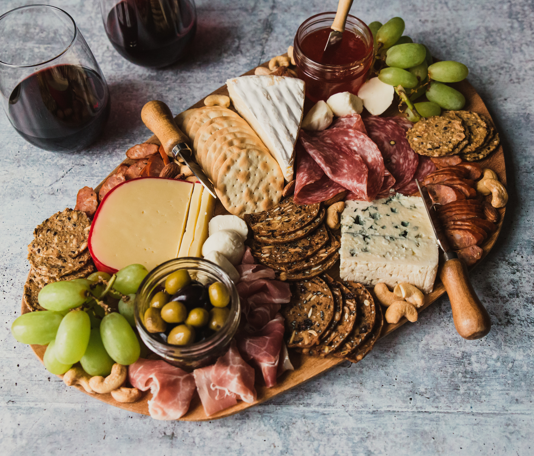 Close up of charcuterie board and glasses of wine on stone counter. 