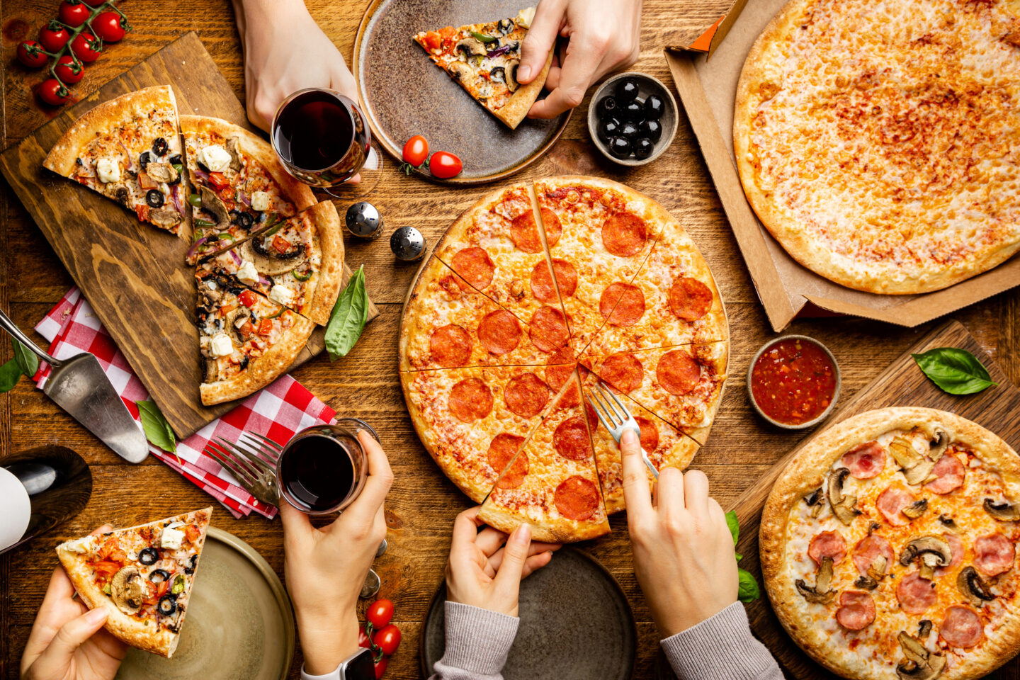 Family or friends pizza party. Flat-lay of people eating different types of pizza and drinking red wine over rustic wooden table, top view.