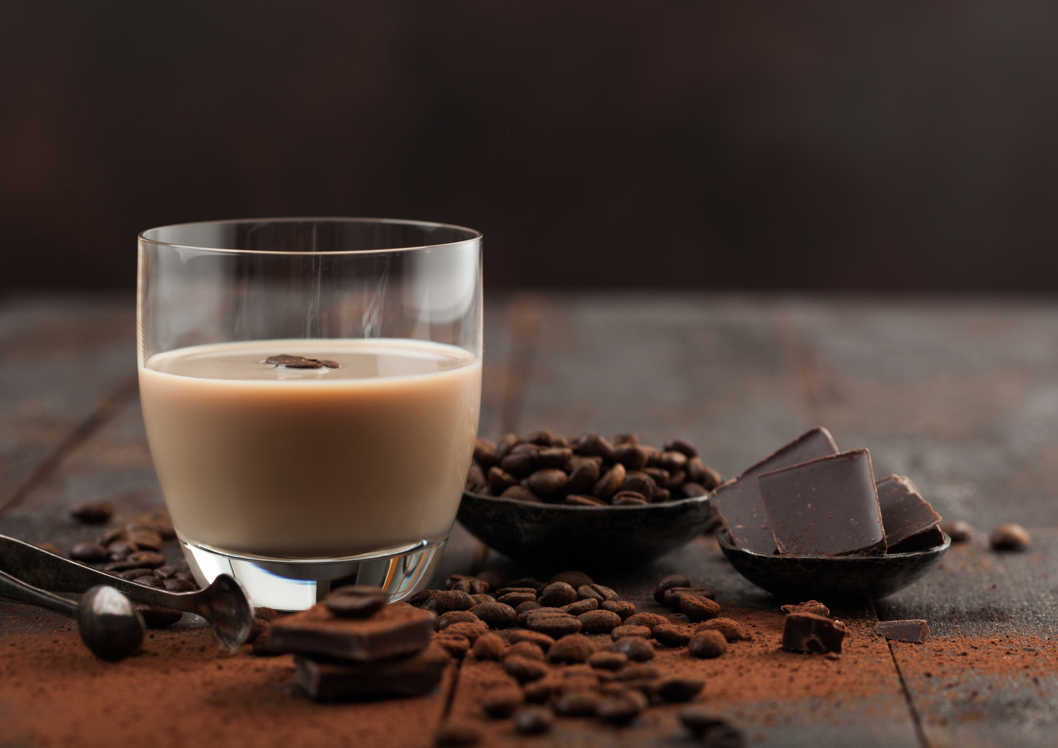 Glass of Irish cream baileys liqueur with coffee beans and powder with dark chocolate on dark wood background. 