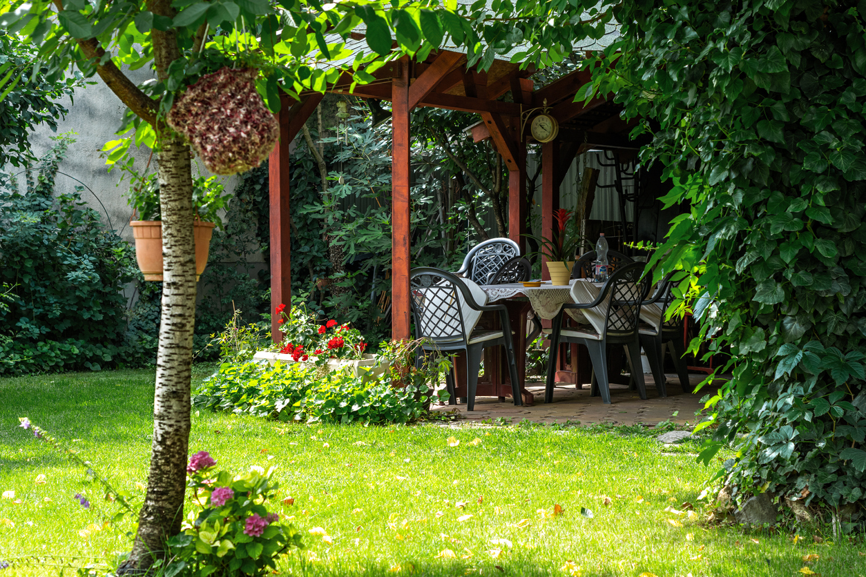 Wooden gazebo with a clock in a shady courtyard garden on a bright summer day.