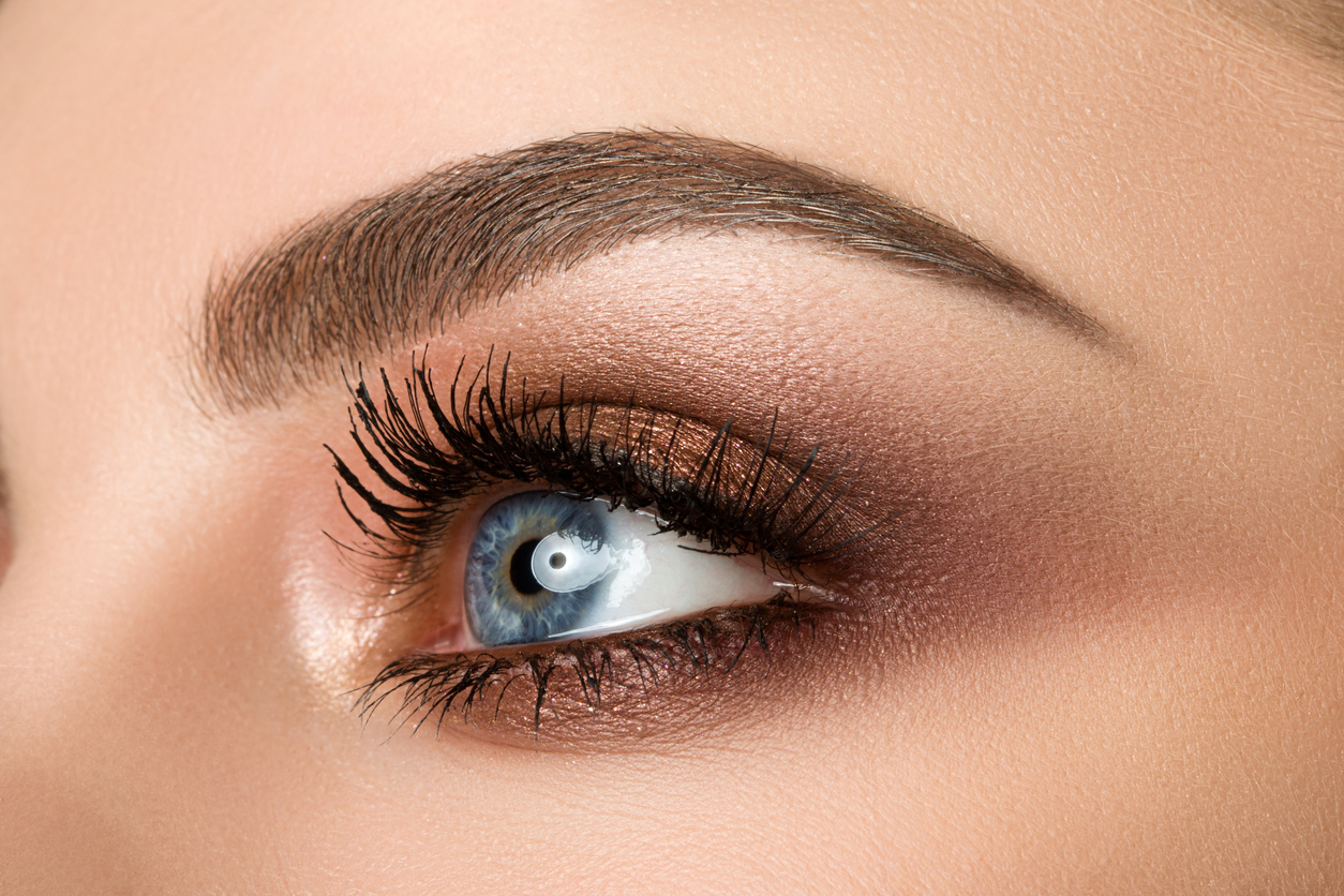 Close up of blue woman eye with beautiful brown with red and orange shades smokey eyes makeup. Modern fashion make up.