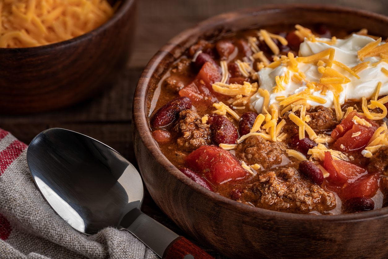 Closeup of bowl of chili with shredded cheddar cheese and sour cream
