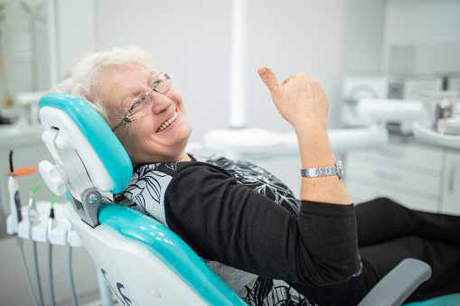 An old senior woman sitting in a dental chair thumb up