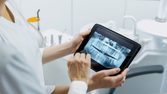 Cropped shot of a professional dentist showing jaws and teeth x-rays to her patient, using a digital tablet technology, discussing a treatment plan.