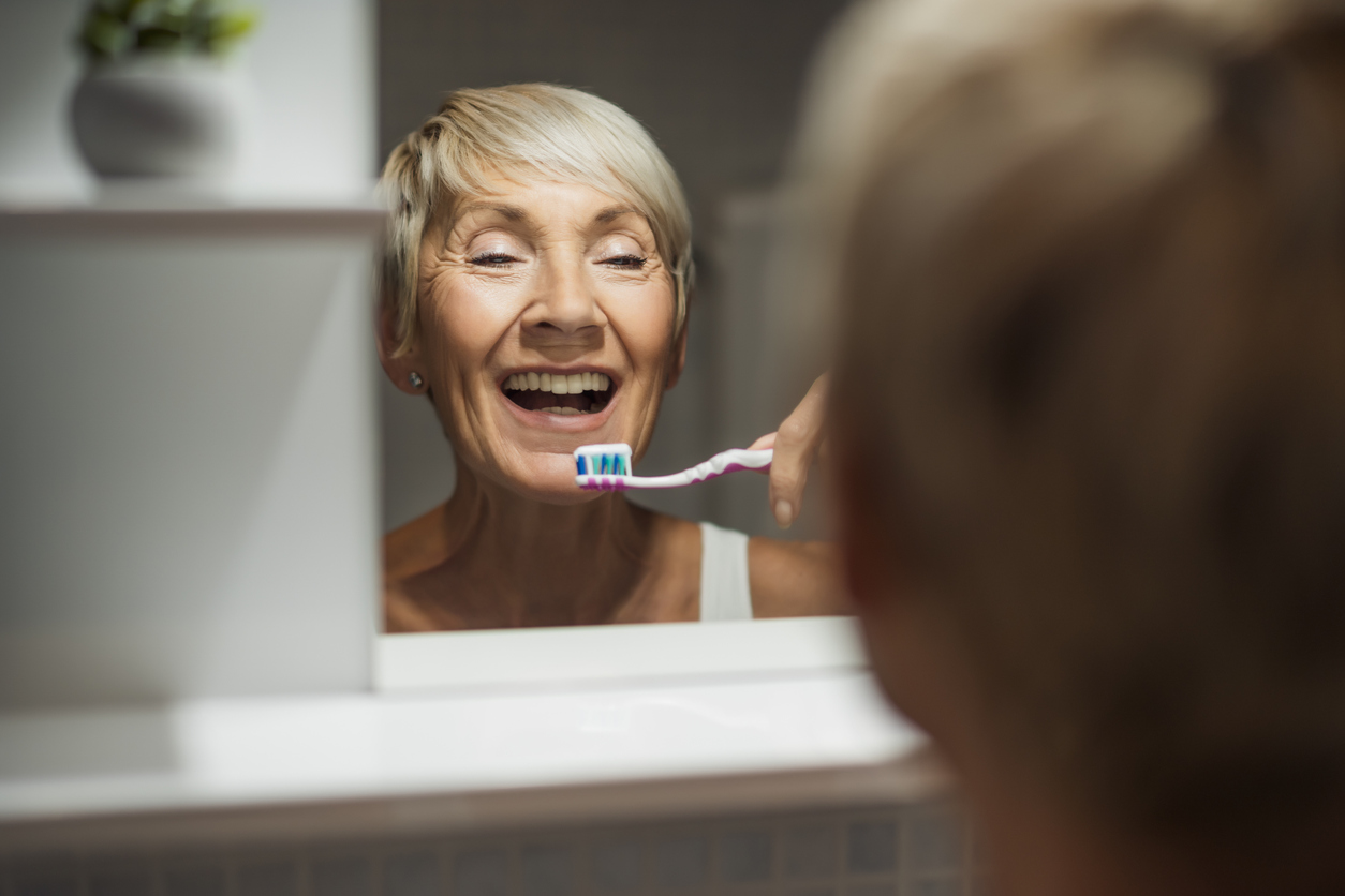 A mature woman is cleaning her teeth in the bathroom.