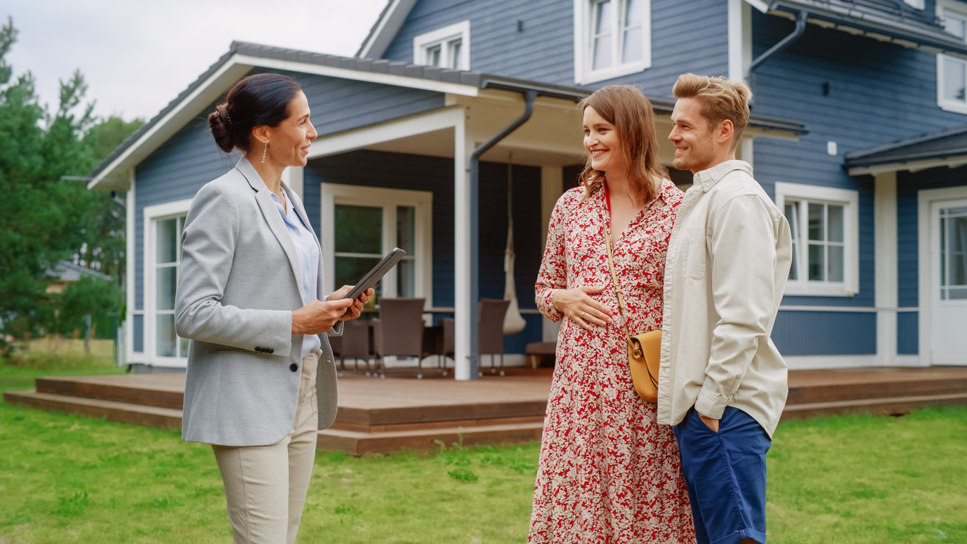 Young Couple Visiting a Potential New Home Property with Professional Real Estate Agent. Female real estate agent Showing the House to Future Homeowners.