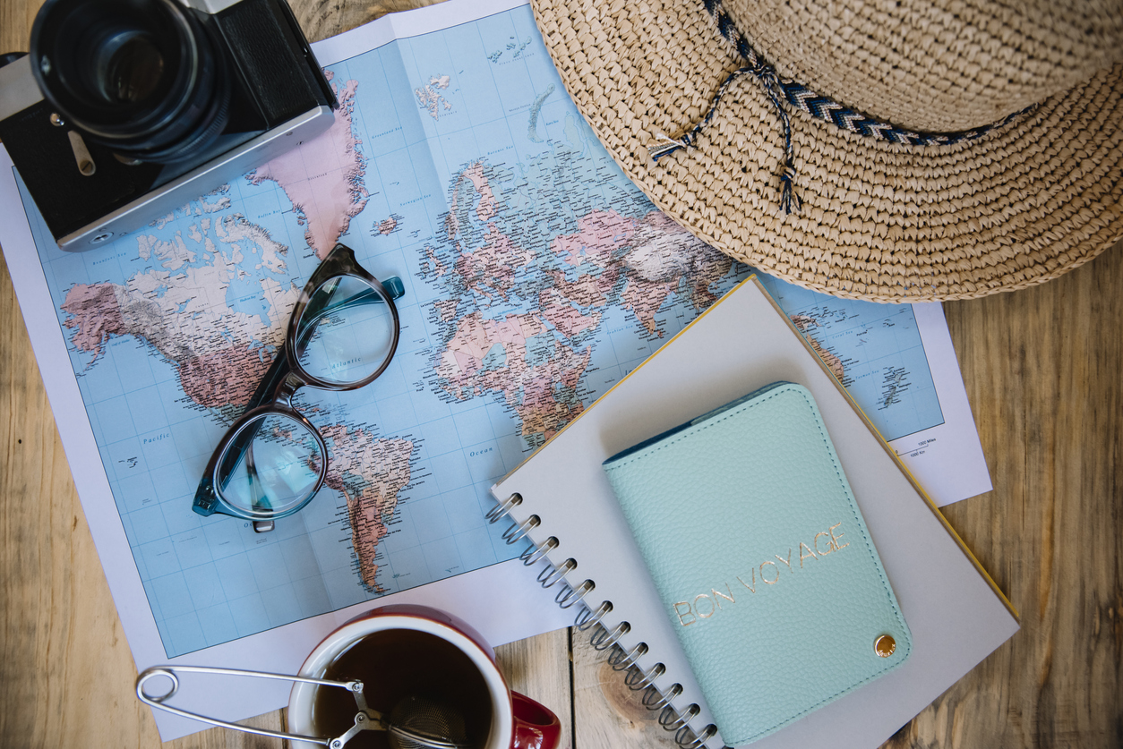 Travel preparations essentials. World map, cup of tea, vintage film camera, hat, passport, notebook and stylish glasses on the old rustic wooden table background, flat lay