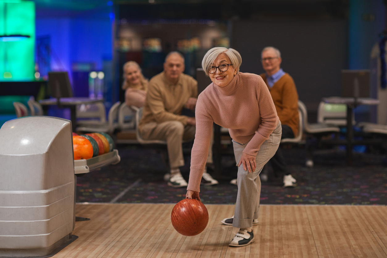 senior woman playing bowling with group of friends 