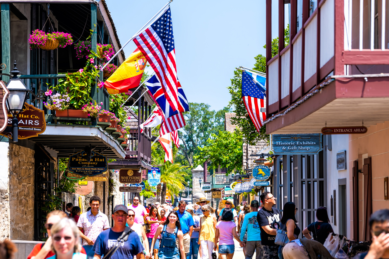 St. Augustine, USA - May 10, 2018: People shopping at Florida city St George Street by stores shops and restaurants in old town city with American and international flags