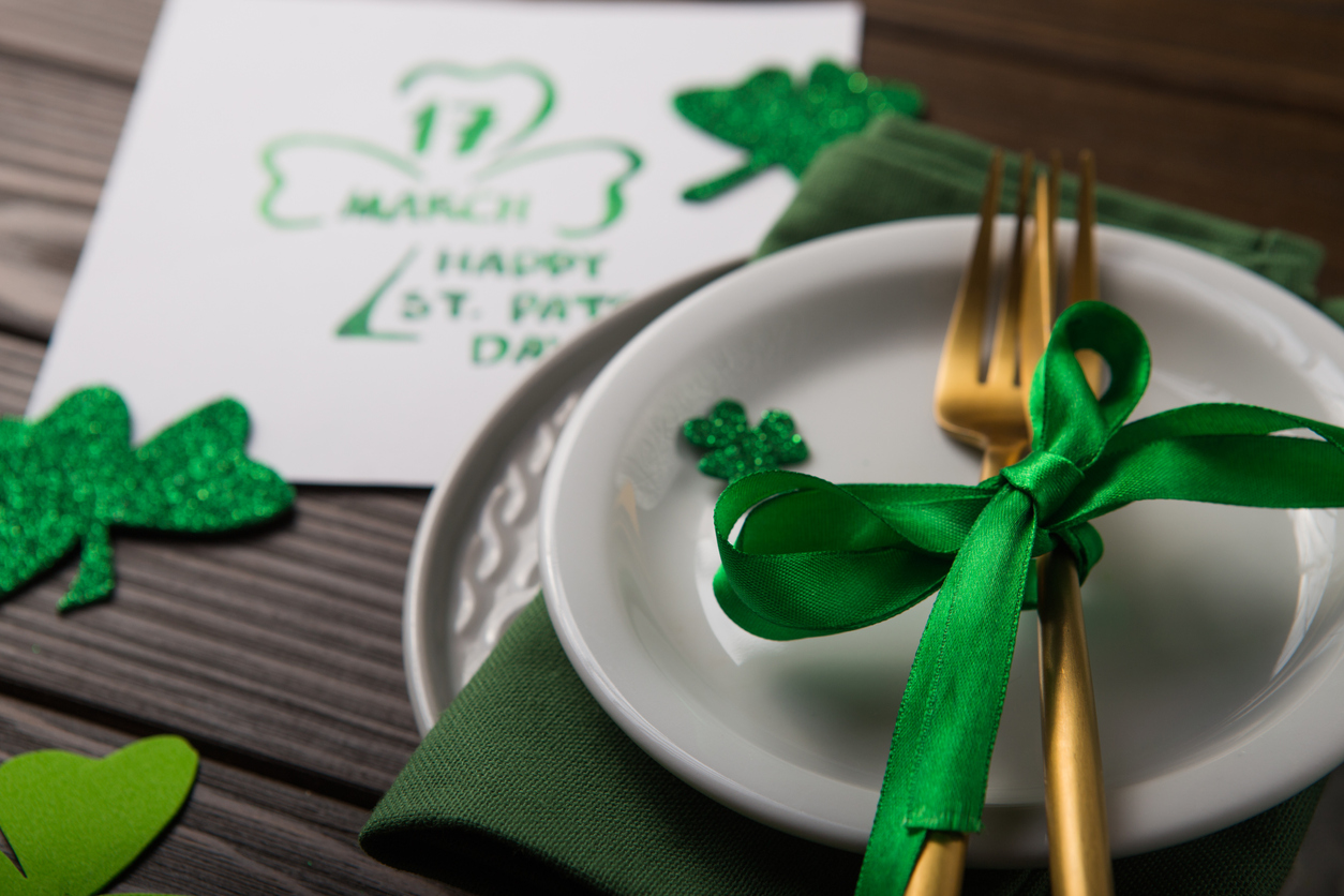 St Patrick's Day party table setting decorated with green leprechaun on wooden background.