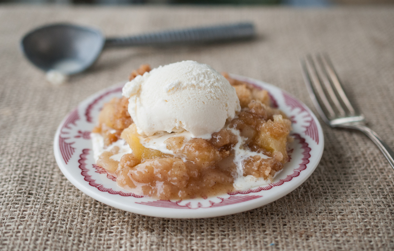 A piece of freshly made warm homemade apple crisp crumble with vanilla ice cream on a red plate. Selective focus with blurred background.