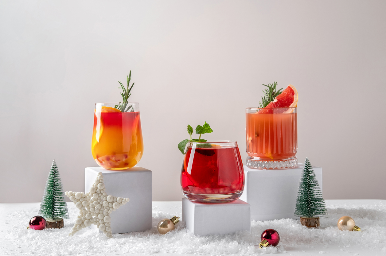 Festive citrus cocktails on podiums. Assortment of fresh Christmas drinks. Pink and red sangria cocktails, pomegranate jingle and citrus tequila smash.