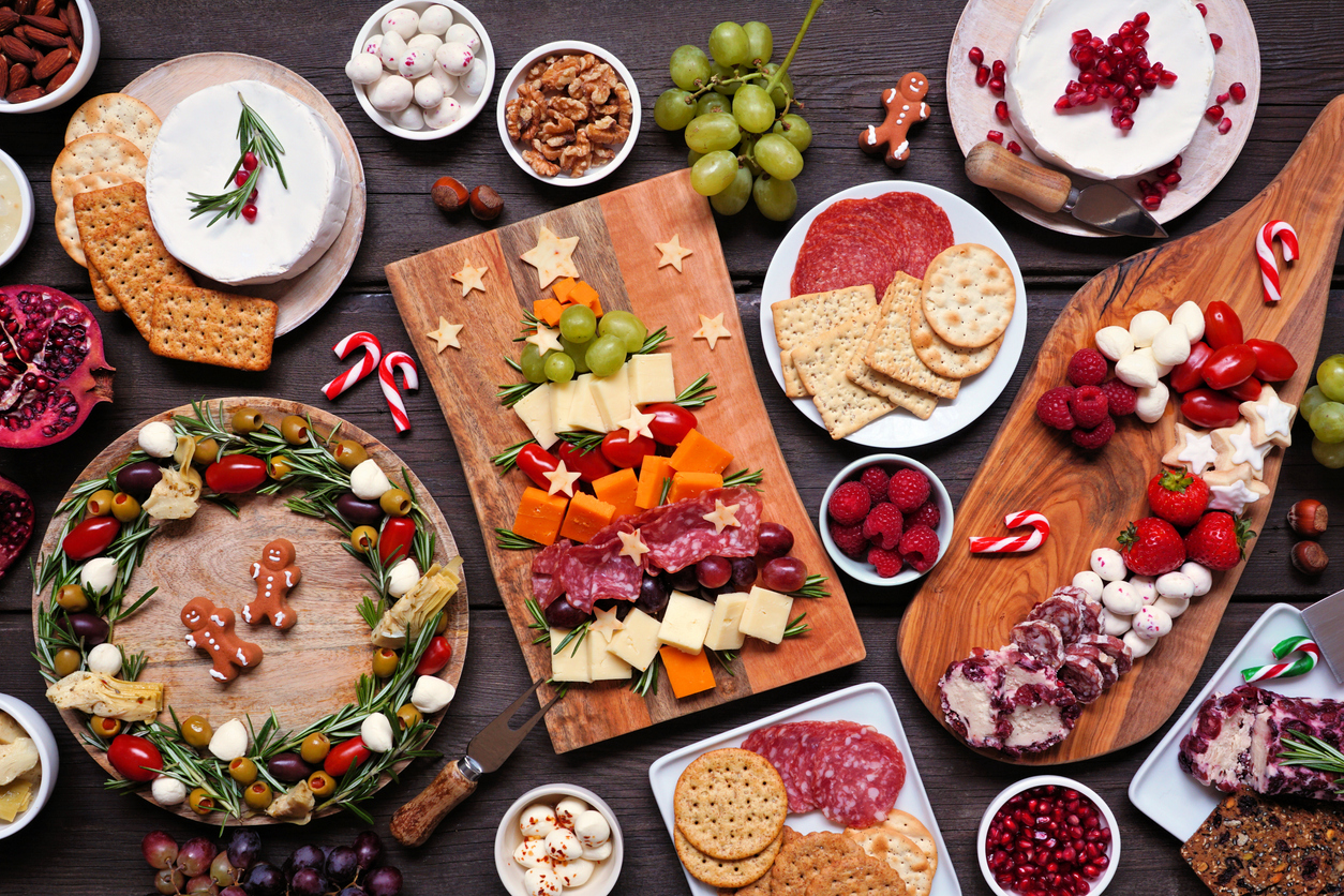 Christmas charcuterie table scene against a dark wood background. Assortment of cheese and meat appetizers. Christmas tree, wreath and candy cane arrangements.