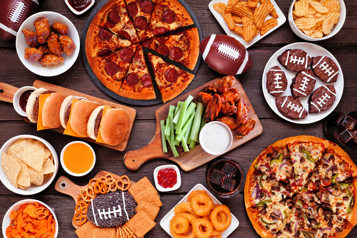 Super Bowl or football theme food table scene. Pizza, hamburgers, wings, snacks and sides.